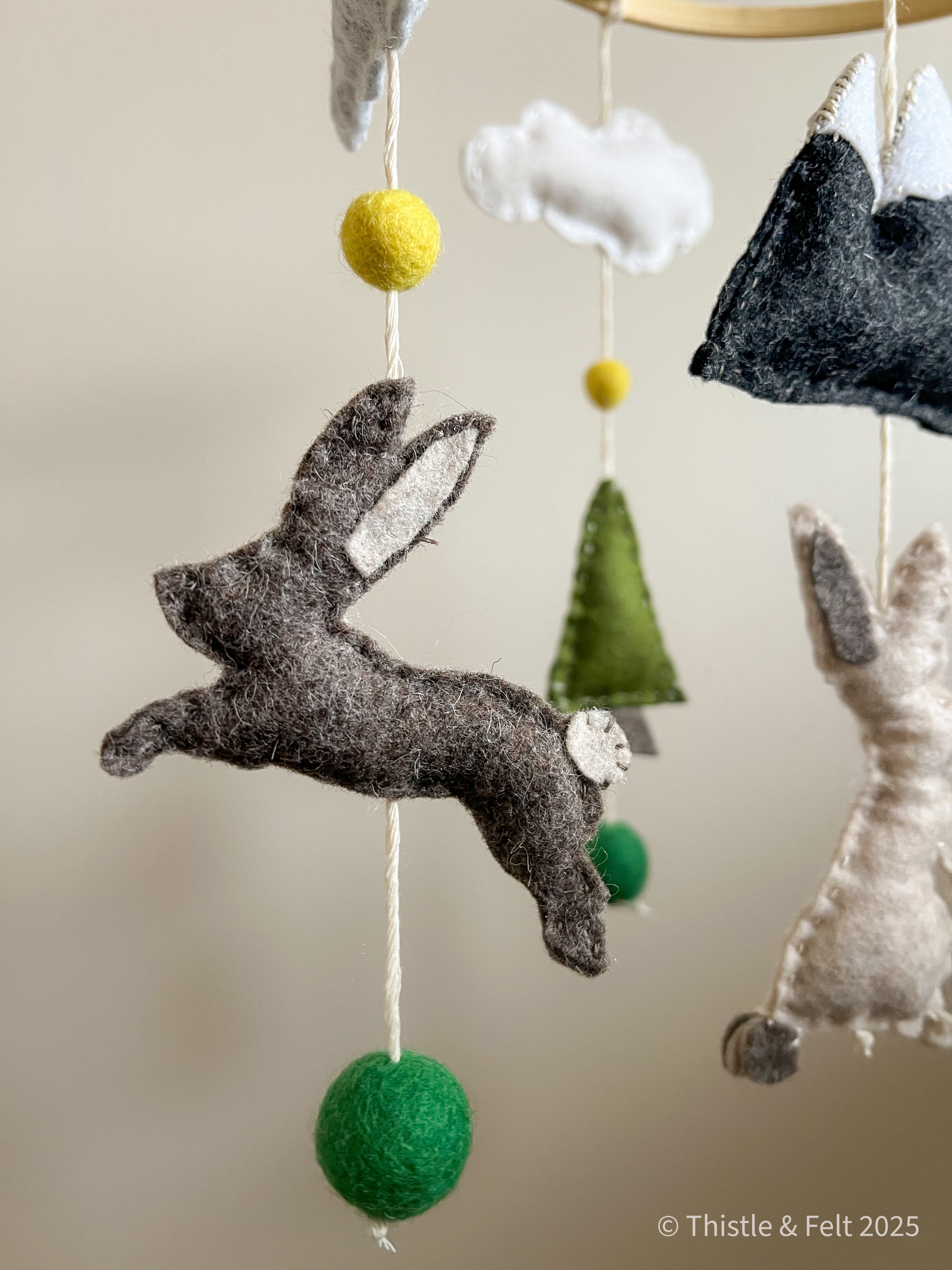 Handmade wool felt baby mobile featuring bunnies among mountain and pine details, with soft natural tone by Thistle & Felt