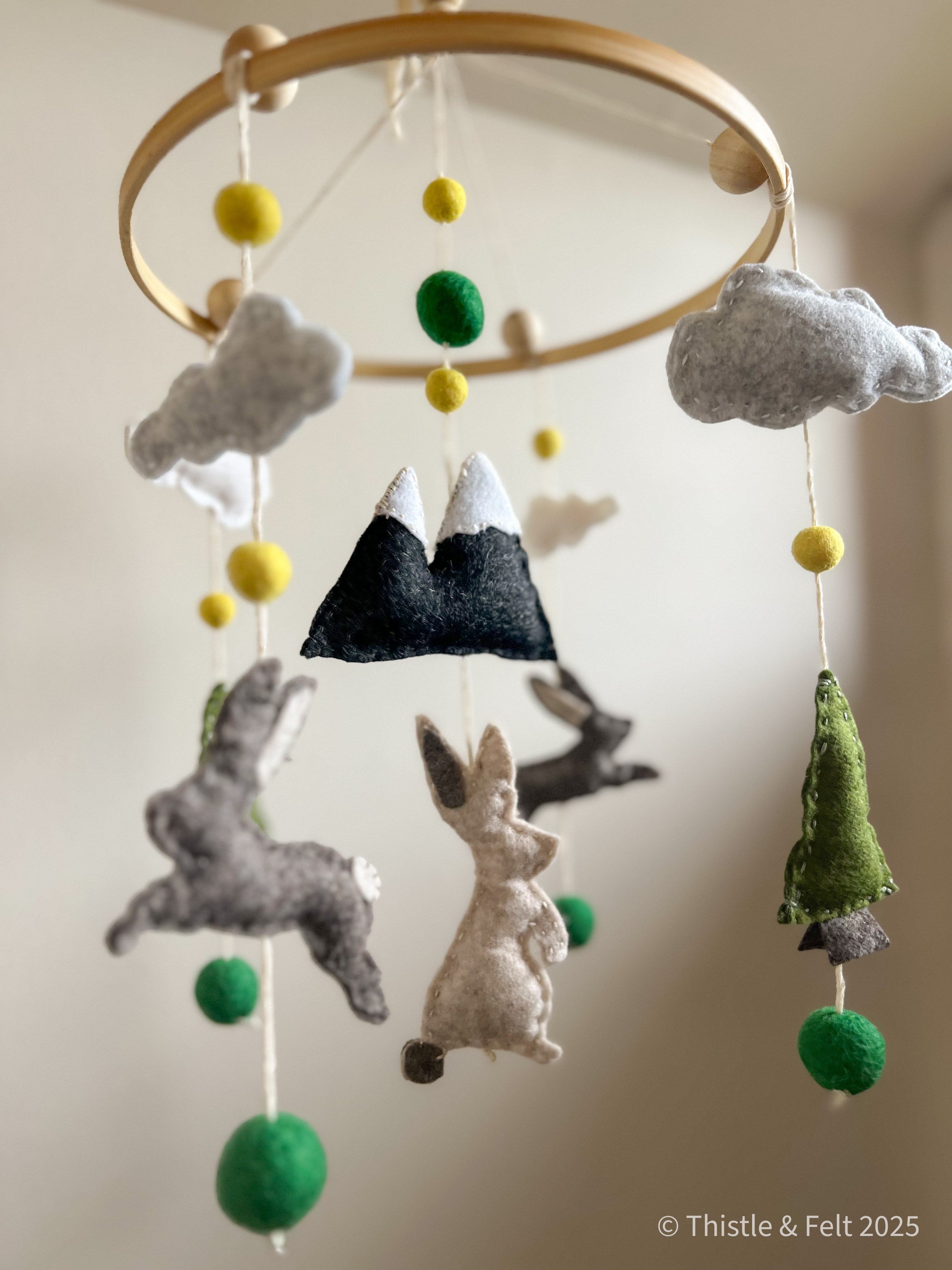 Handmade wool felt baby mobile featuring bunnies among mountain and pine details, with soft natural tone by Thistle & Felt