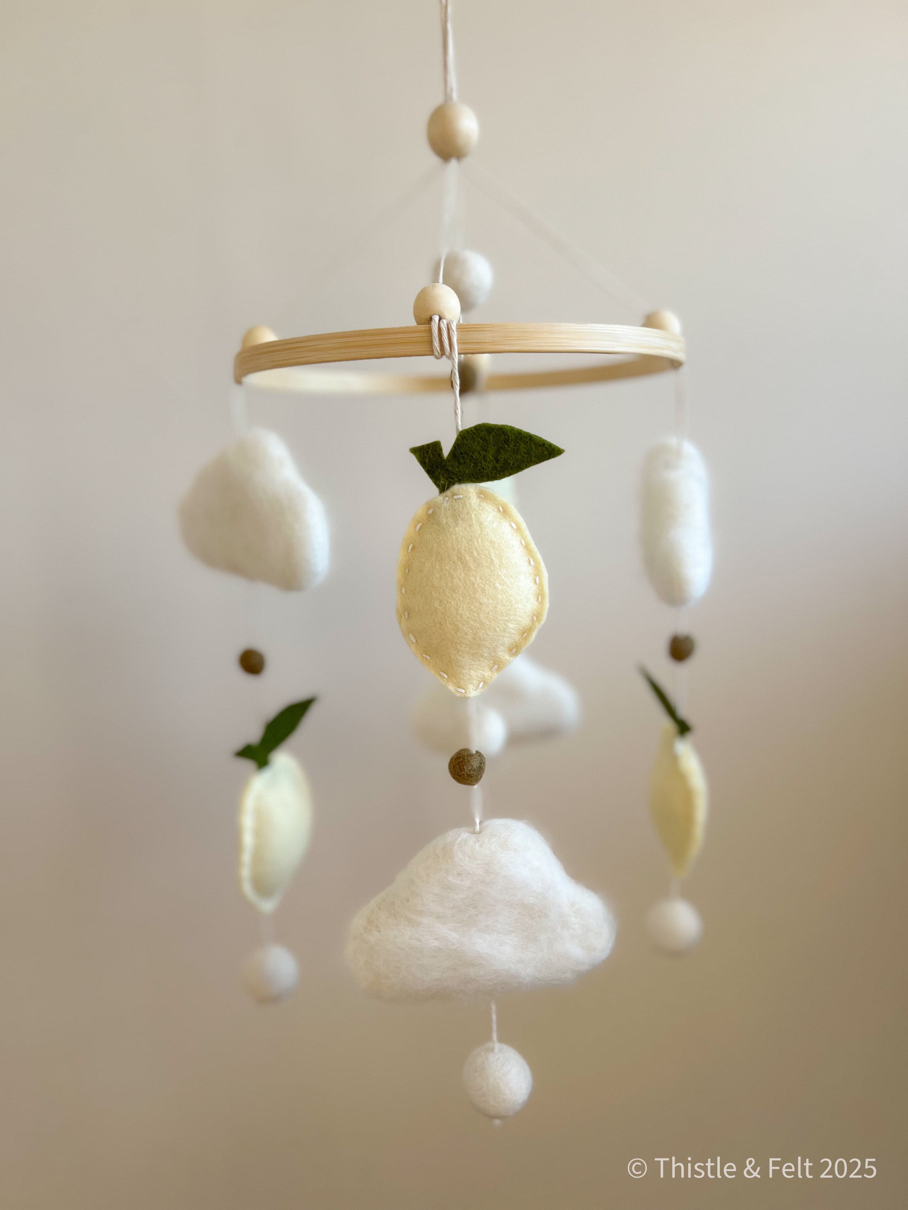 Handmade wool felt lemon nursery mobile with fluffy clouds by Thistle & Felt, perfect for natural nursery décor.