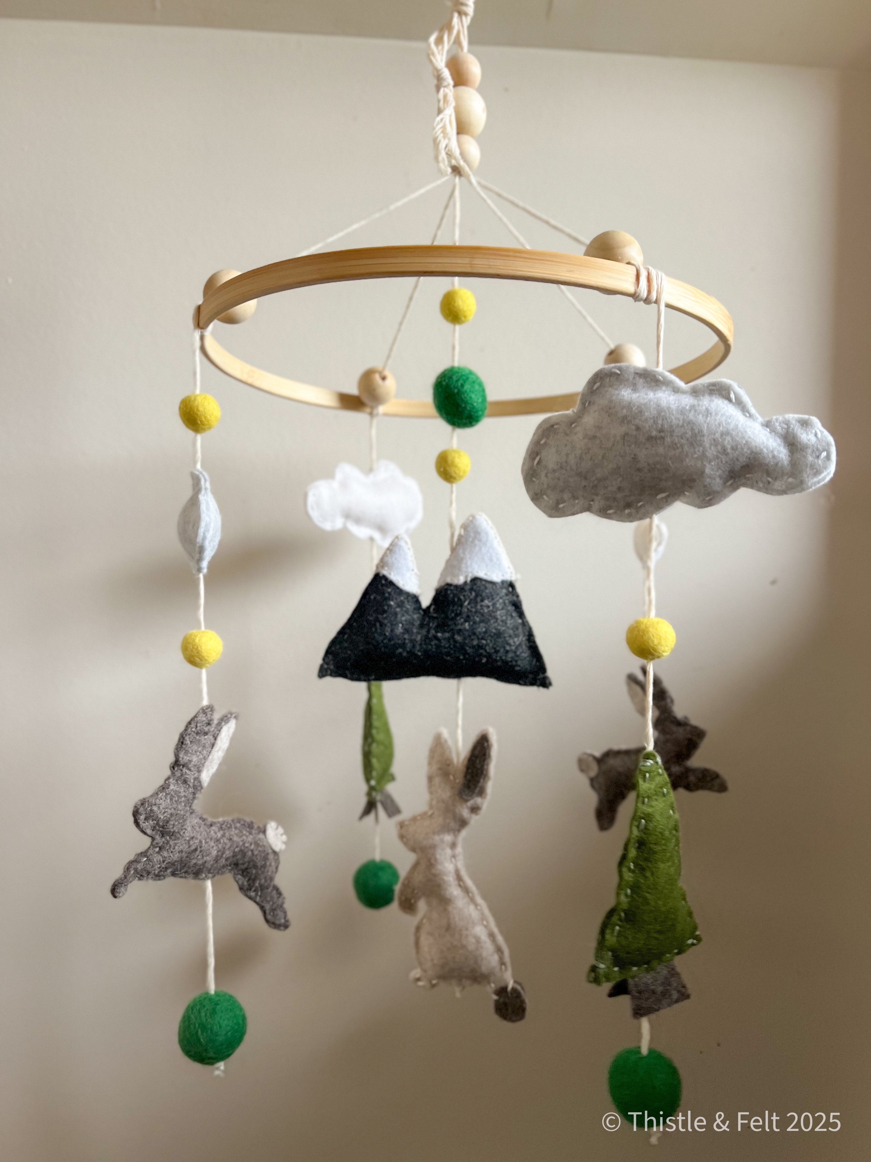 Handmade wool felt baby mobile featuring bunnies among mountain and pine details, with soft natural tone by Thistle & Felt