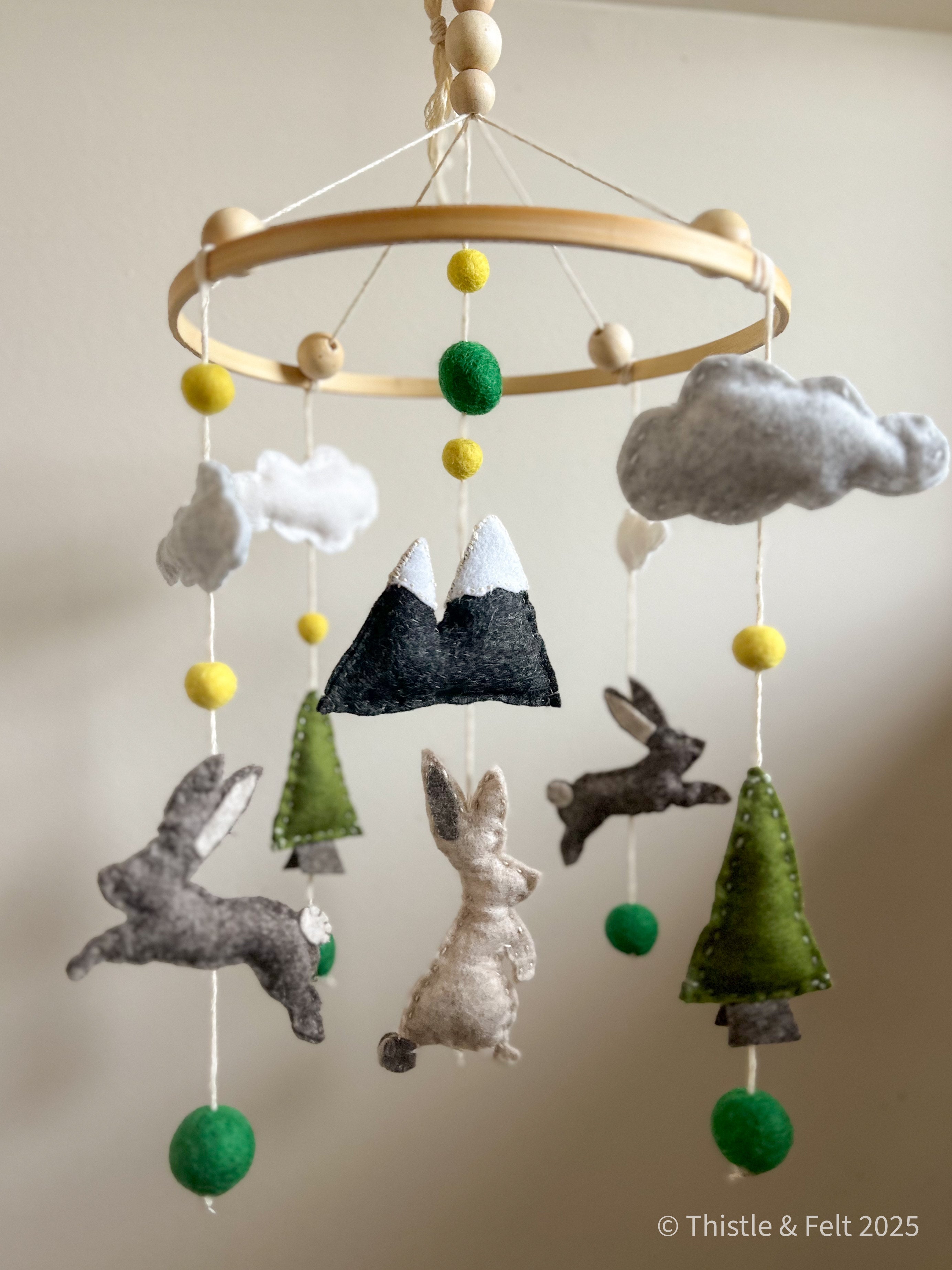Handmade wool felt baby mobile featuring bunnies among mountain and pine details, with soft natural tone by Thistle & Felt