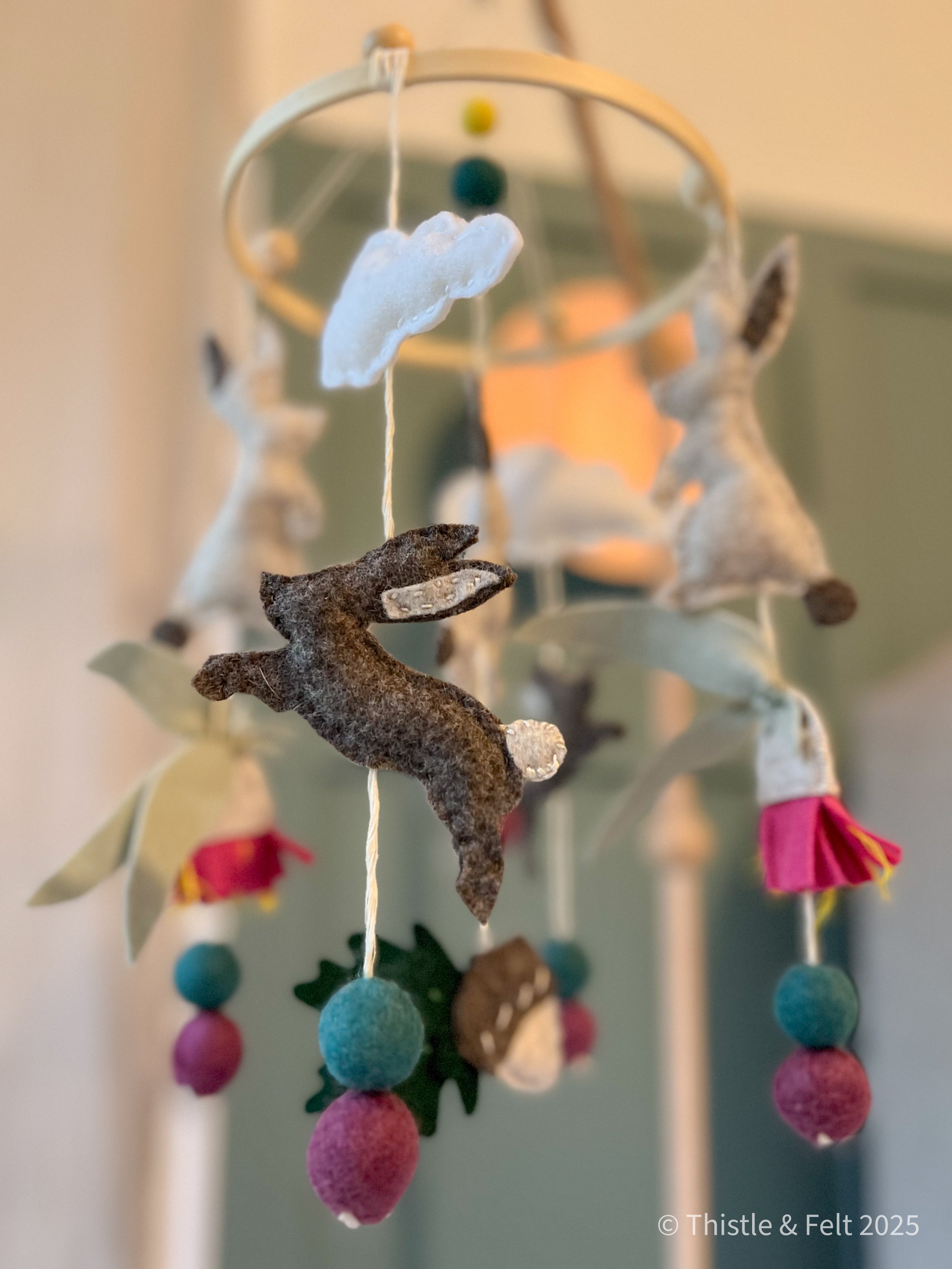 Pure wool felt nursery mobile with woodland bunnies and soft earthy colours, finished with a bamboo hoop by Thistle & Felt